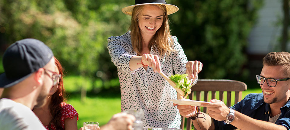 leisure, holidays, eating, people and food concept - happy friends having dinner and sharing salad at summer garden party